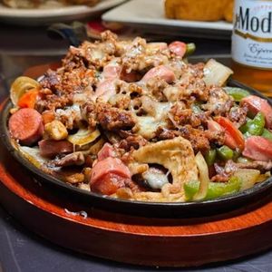 Sizzling skillet of loaded nachos with beef, tomatoes, peppers, and melted cheese on a wooden base