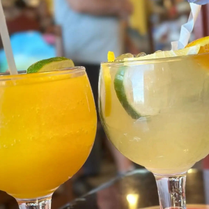 Two colorful cocktails with lime wedges in stemmed glasses on a table