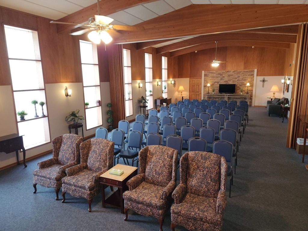 Interior of a funeral home chapel with rows of chairs and decorative armchairs.