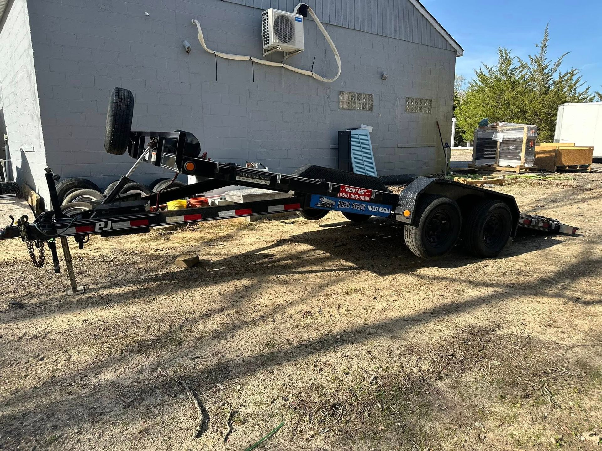 A black boat trailer sitting on dirt in front of a gray building.