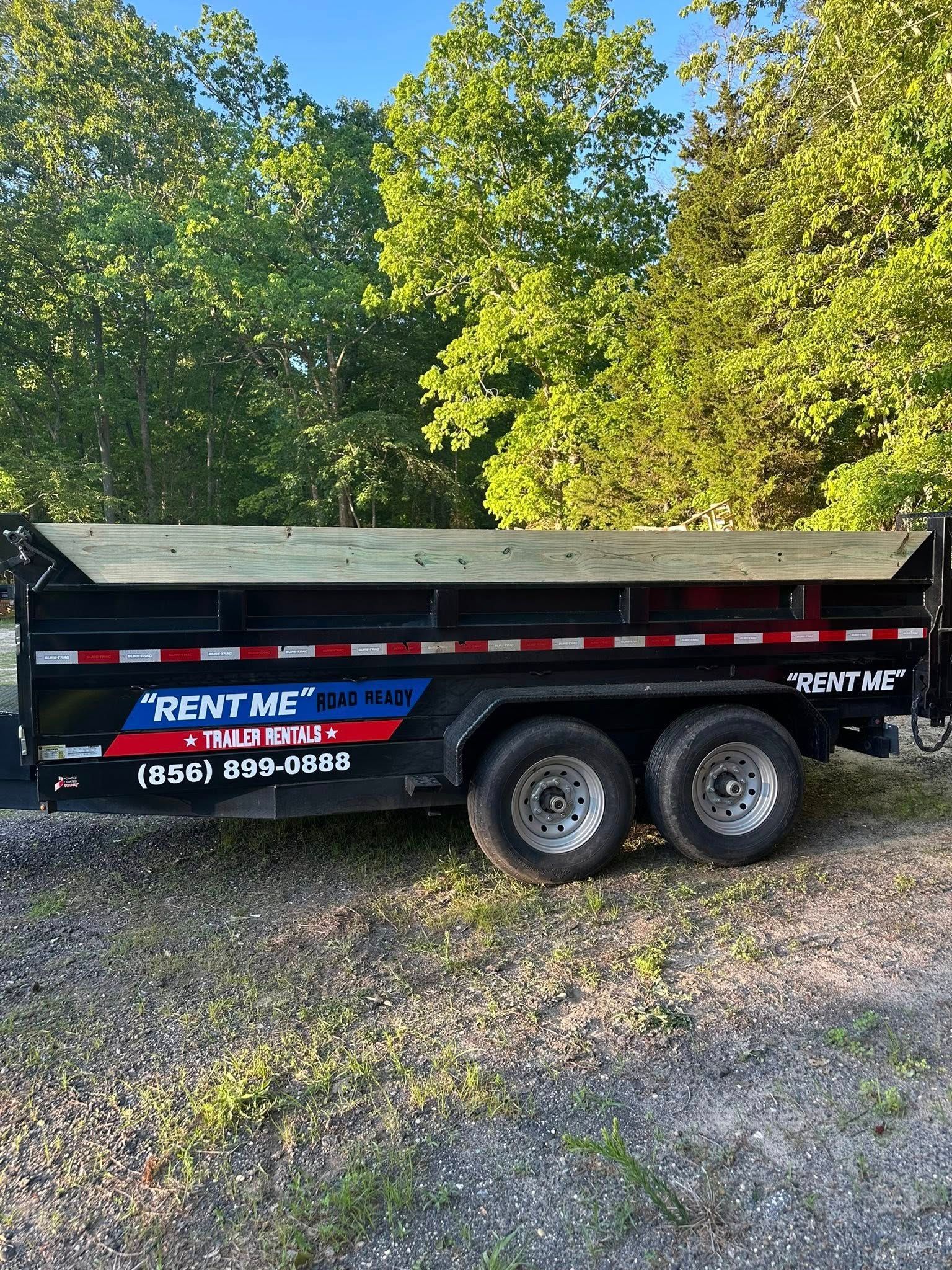 A black dump trailer parked on gravel, with 