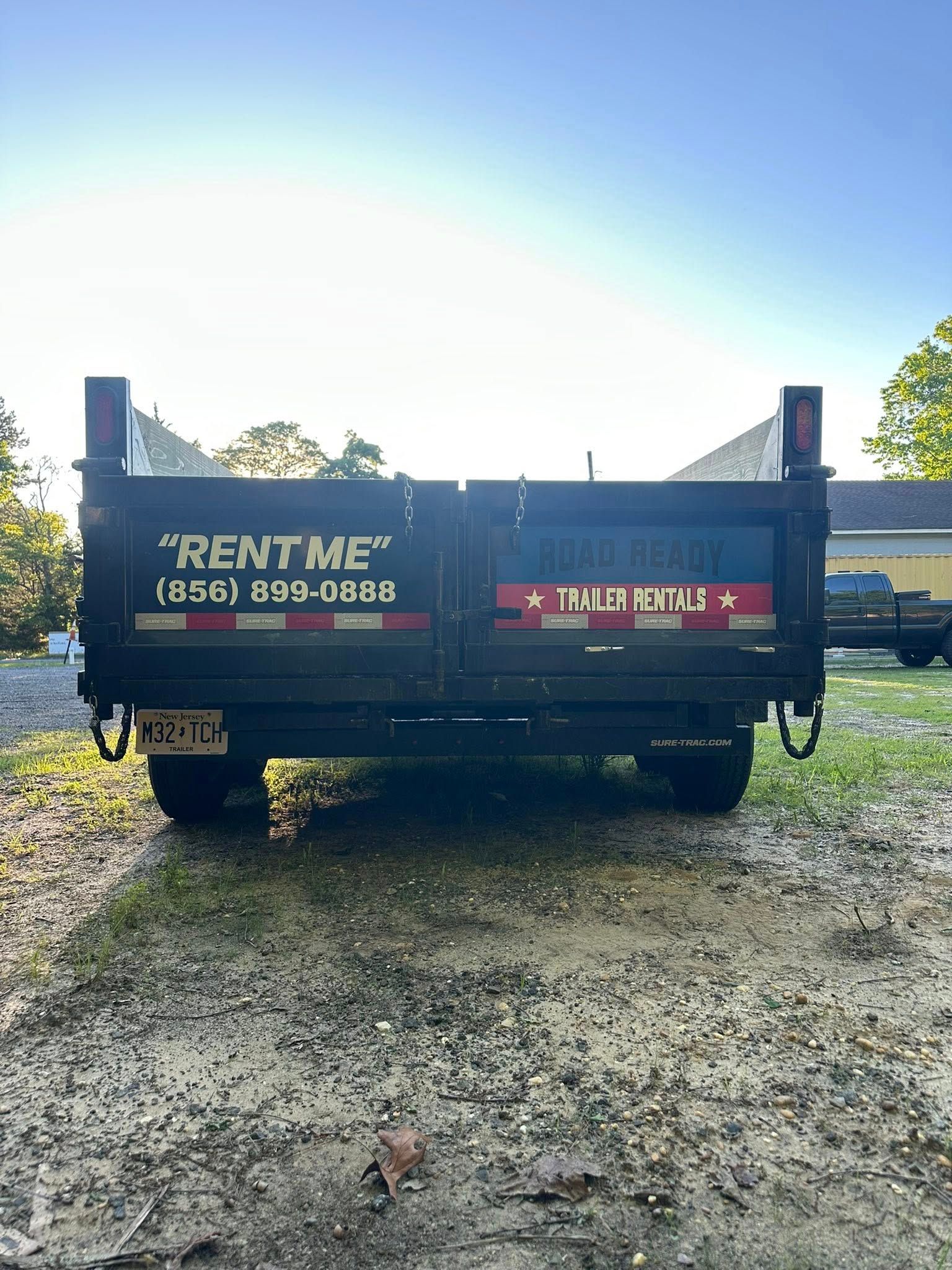 A black dump trailer parked on gravel, featuring 