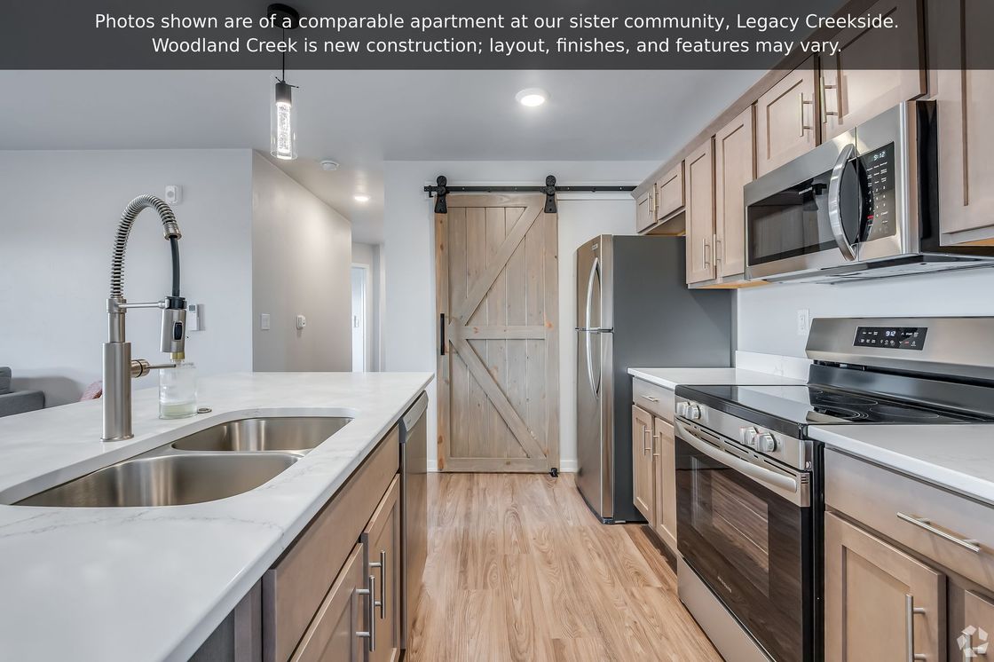 Modern kitchen with white countertops, stainless appliances, wood floors, and farmhouse sliding pantry door