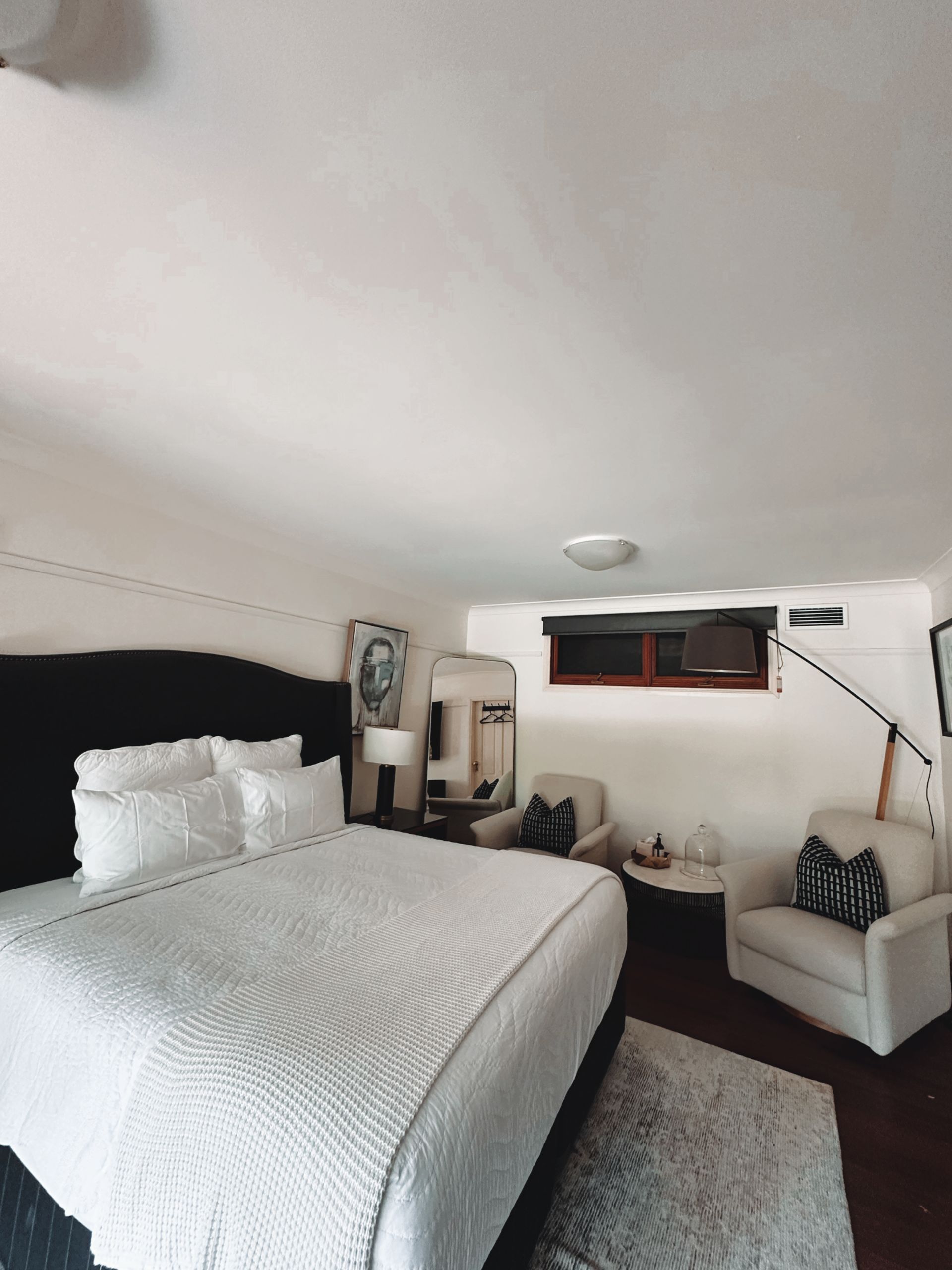 Bedroom with a large bed, two armchairs, a rug, and a mirror. White and black decor, small window — Integral Cleaning Services in Aberdare, NSW