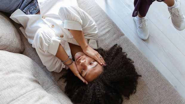 A woman is laying on a couch with her head on her hands.