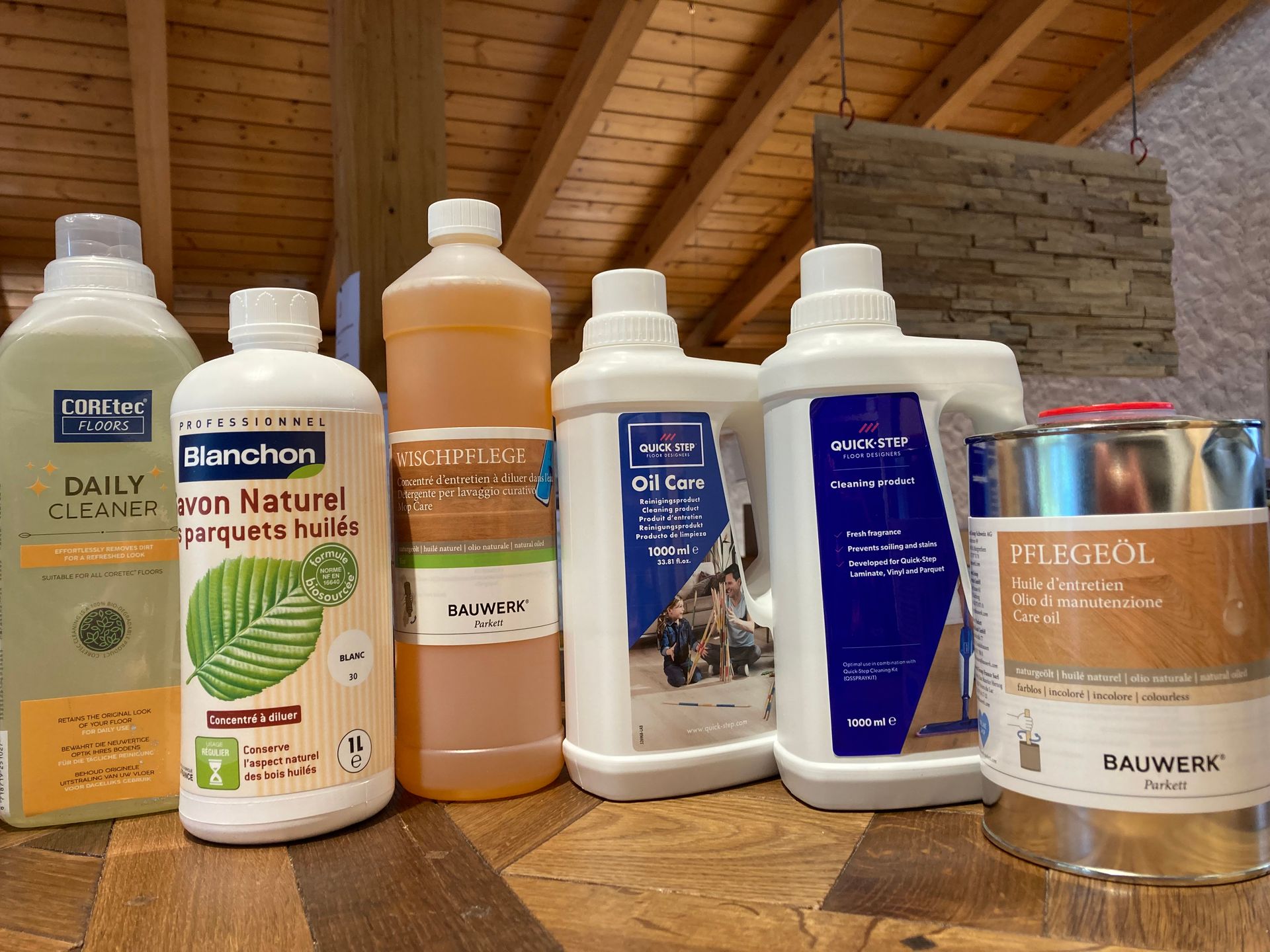 Assortiment de produits d'entretien pour sols avec marques COREtec, Blanchon, Bauwerk, et Quick-Step disposés sur un comptoir en bois