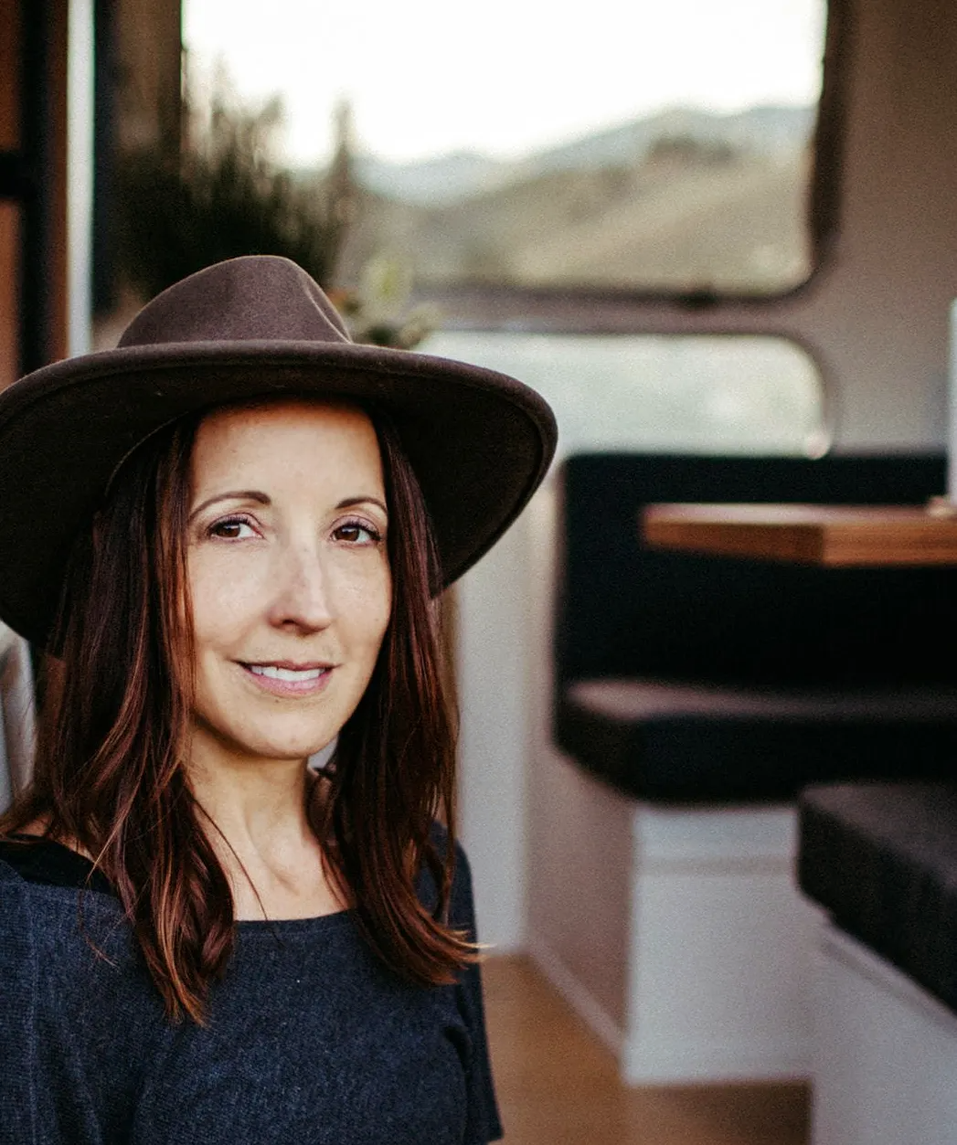 Photo of a woman with dark brown hair wearing a brown suede wide brimmed hat smiling