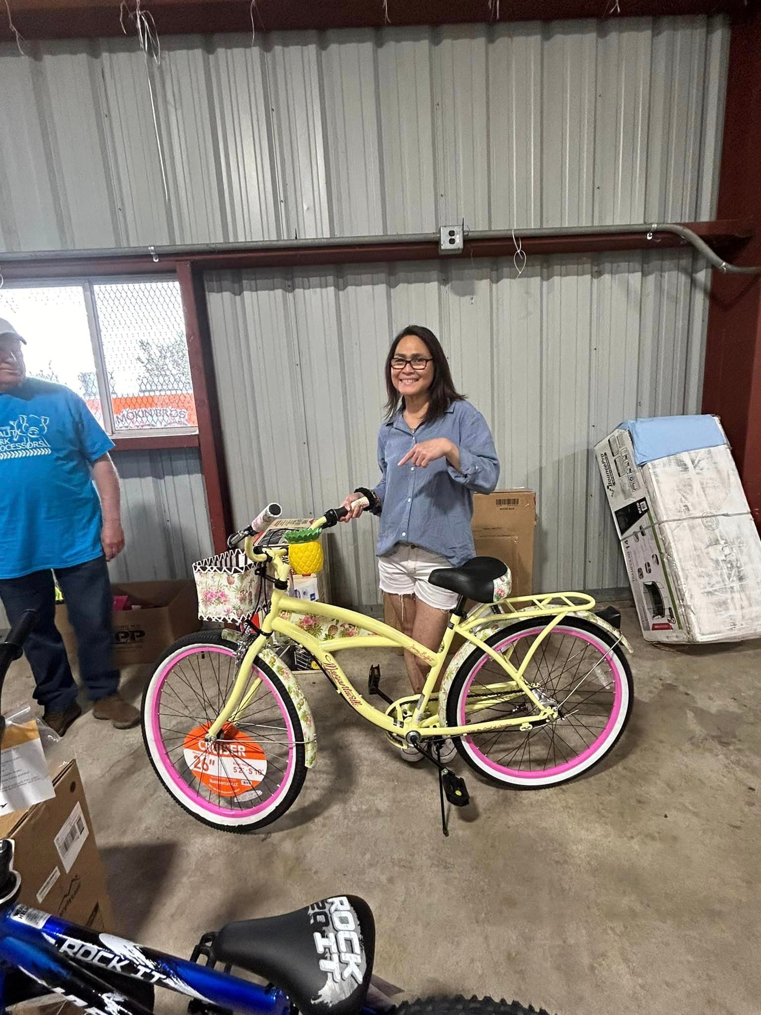 A person smiles while pointing at a yellow bicycle with pink rims and a white basket inside a storage area.