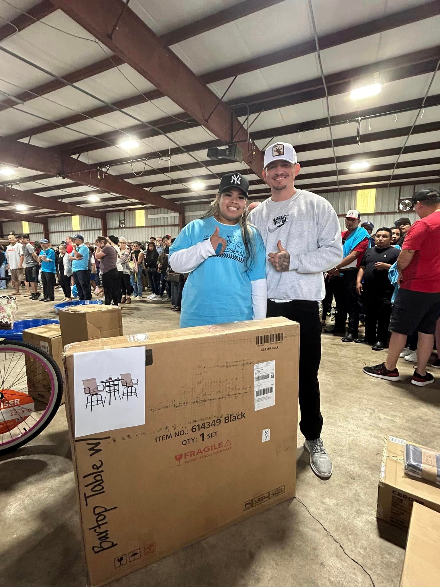 A person in a blue shirt and a person in a white sweatshirt pose behind a large cardboard box in an indoor event space.