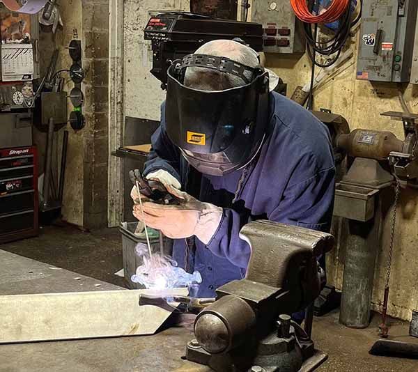 A person wearing a welding helmet uses a torch to weld metal in a workshop.
