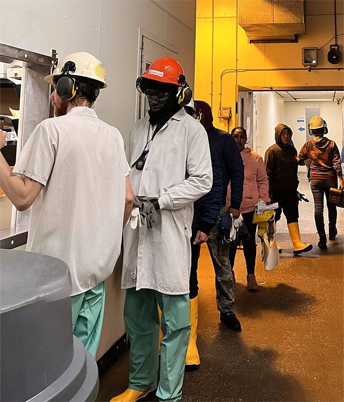 A group of workers in protective gear, including hard hats and yellow boots, stands in a hallway line.