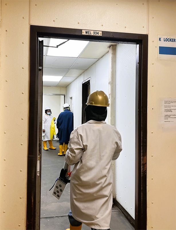 Personnel in protective gear and helmets walk through a doorway into a white industrial corridor.