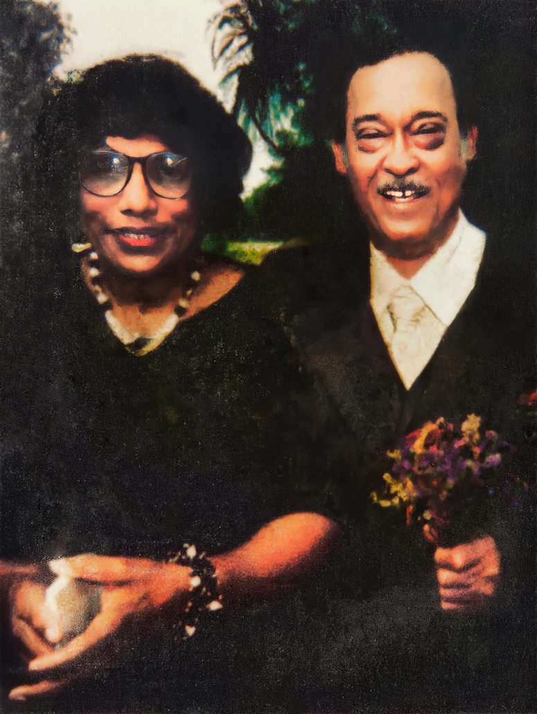 Two people posing indoors, one holding flowers, both in dark clothing and smiling.
