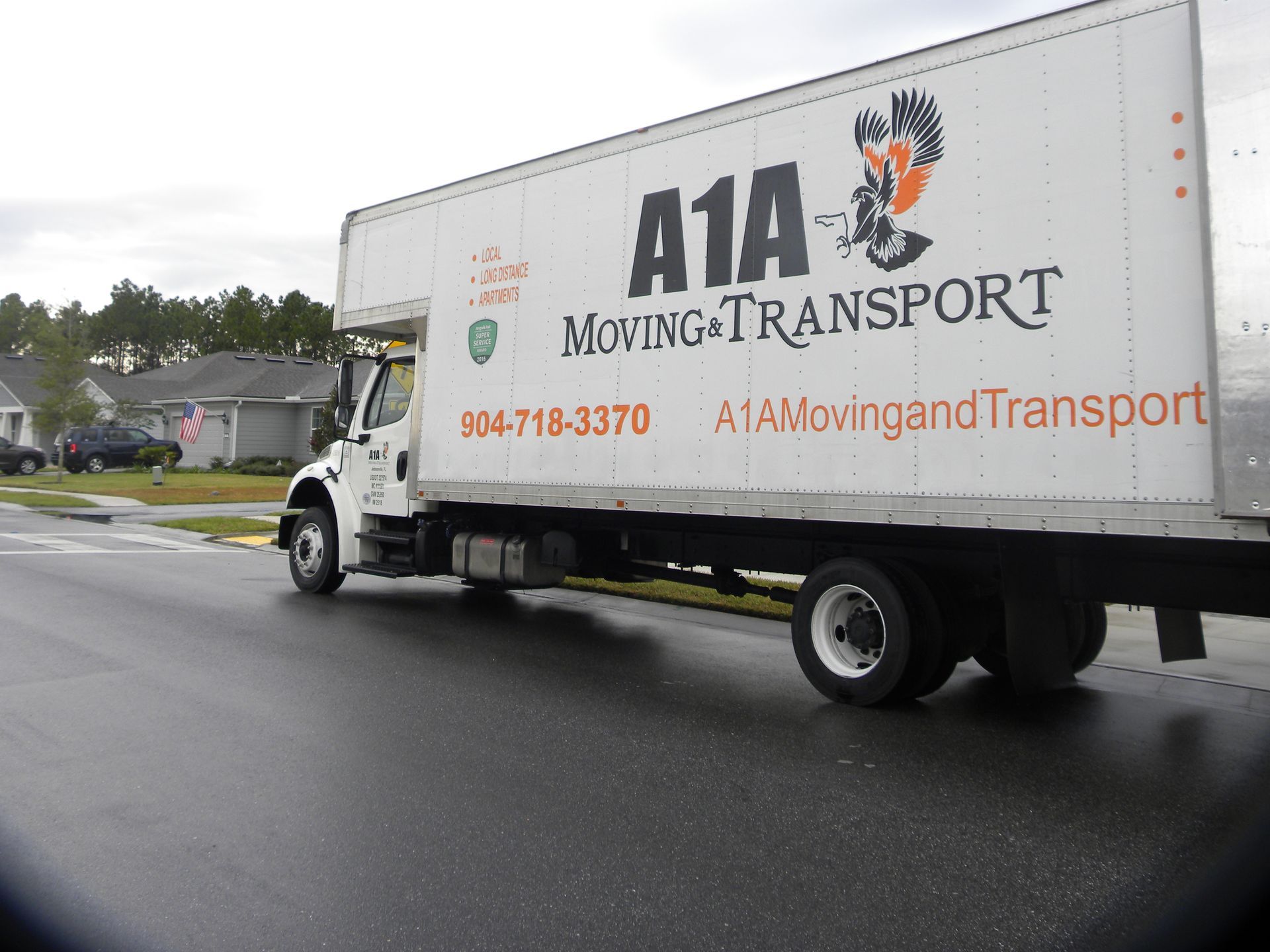 Sandblasting and Rust Removal in Harford County, MD White A1A Moving & Transport truck on a wet road in front of houses; cloudy sky.