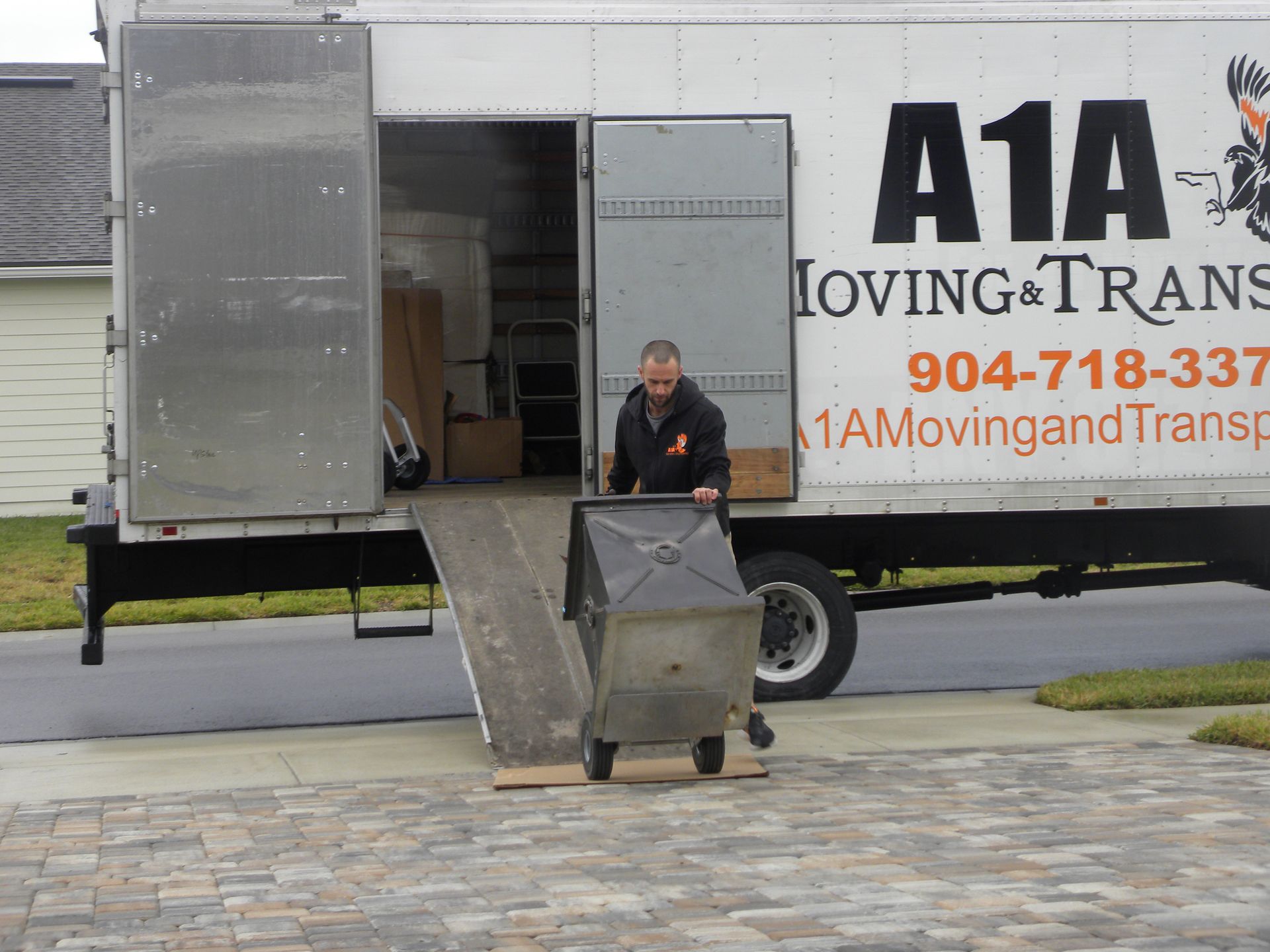Storage Near You in Jacksonville, FL Man rolling a grill on a dolly out of a moving truck with ramp; truck has company logo.