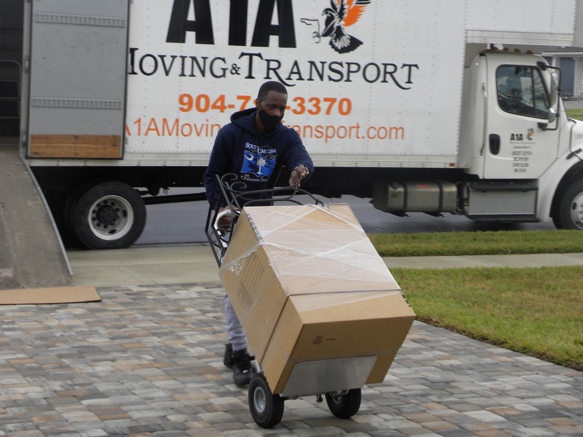 Sandblasting and Rust Removal in Harford County, MD Man in mask moving large box on a dolly to moving truck; parked on a driveway.