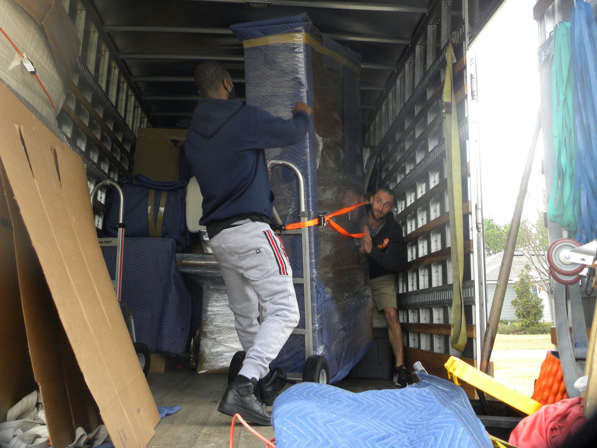 Sandblasting and Rust Removal in Harford County, MD Two people loading a wrapped tall item into a moving truck. The truck's interior is visible.