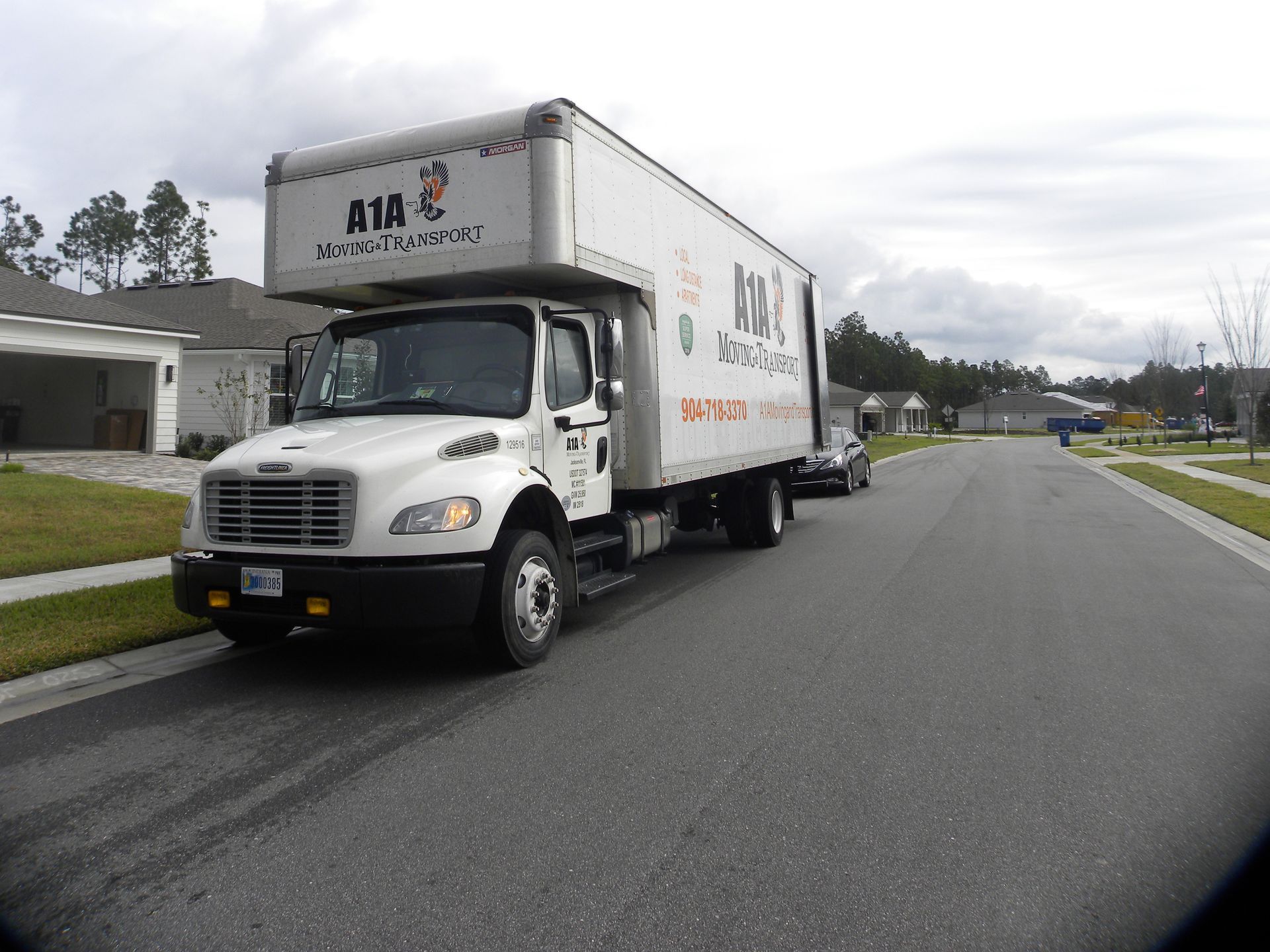 Three people loading a large, wrapped item onto a moving truck in a residential street.