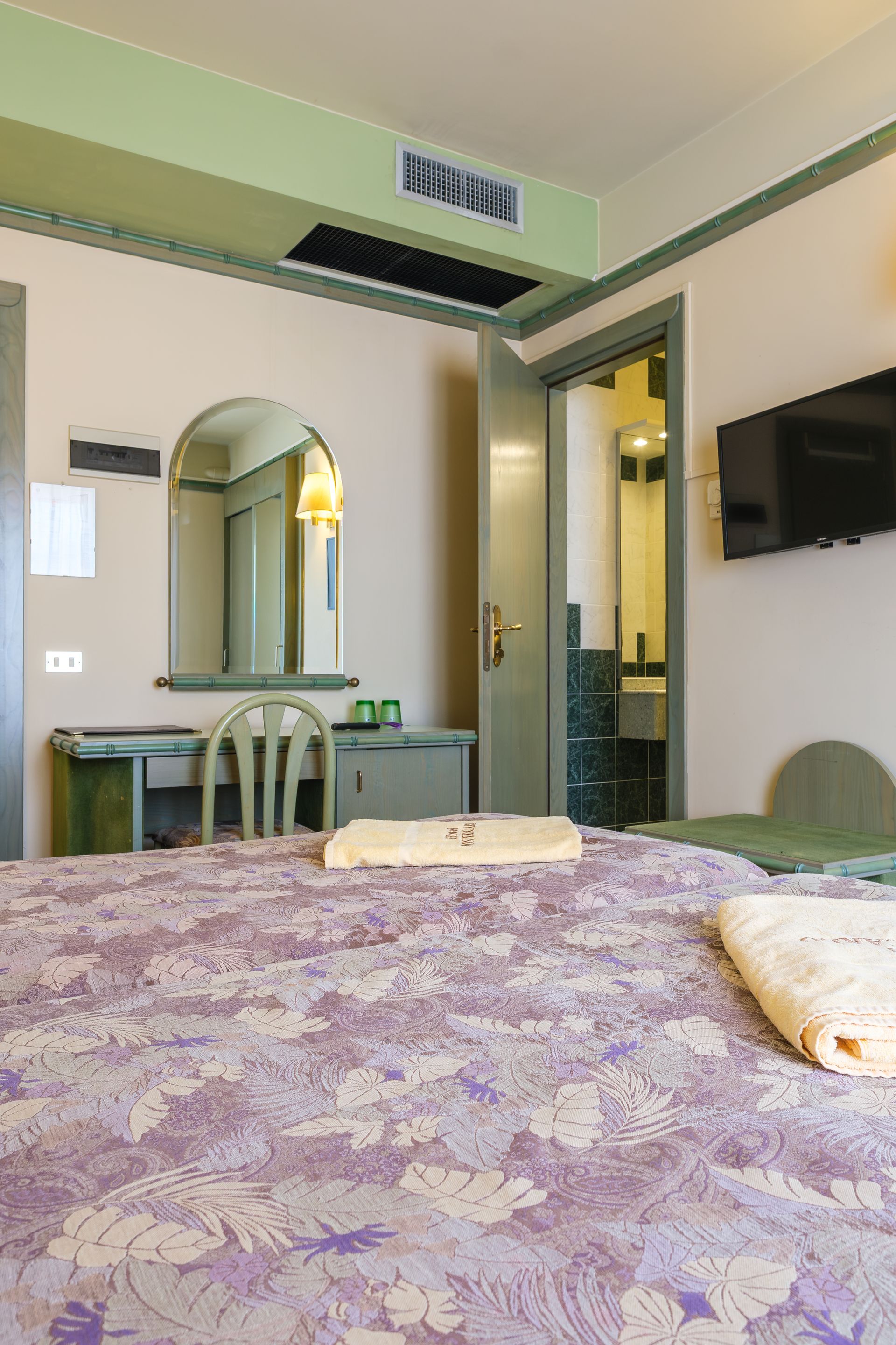 Una camera d'albergo con un letto, una scrivania, sedie e una televisione.