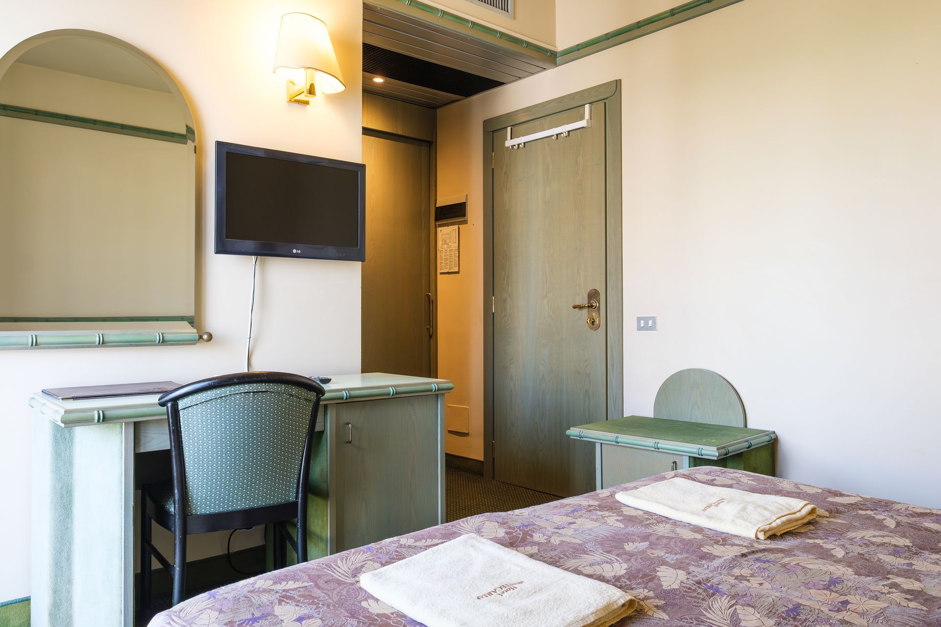 Una camera d'albergo con un letto, una scrivania, una sedia e una televisione.