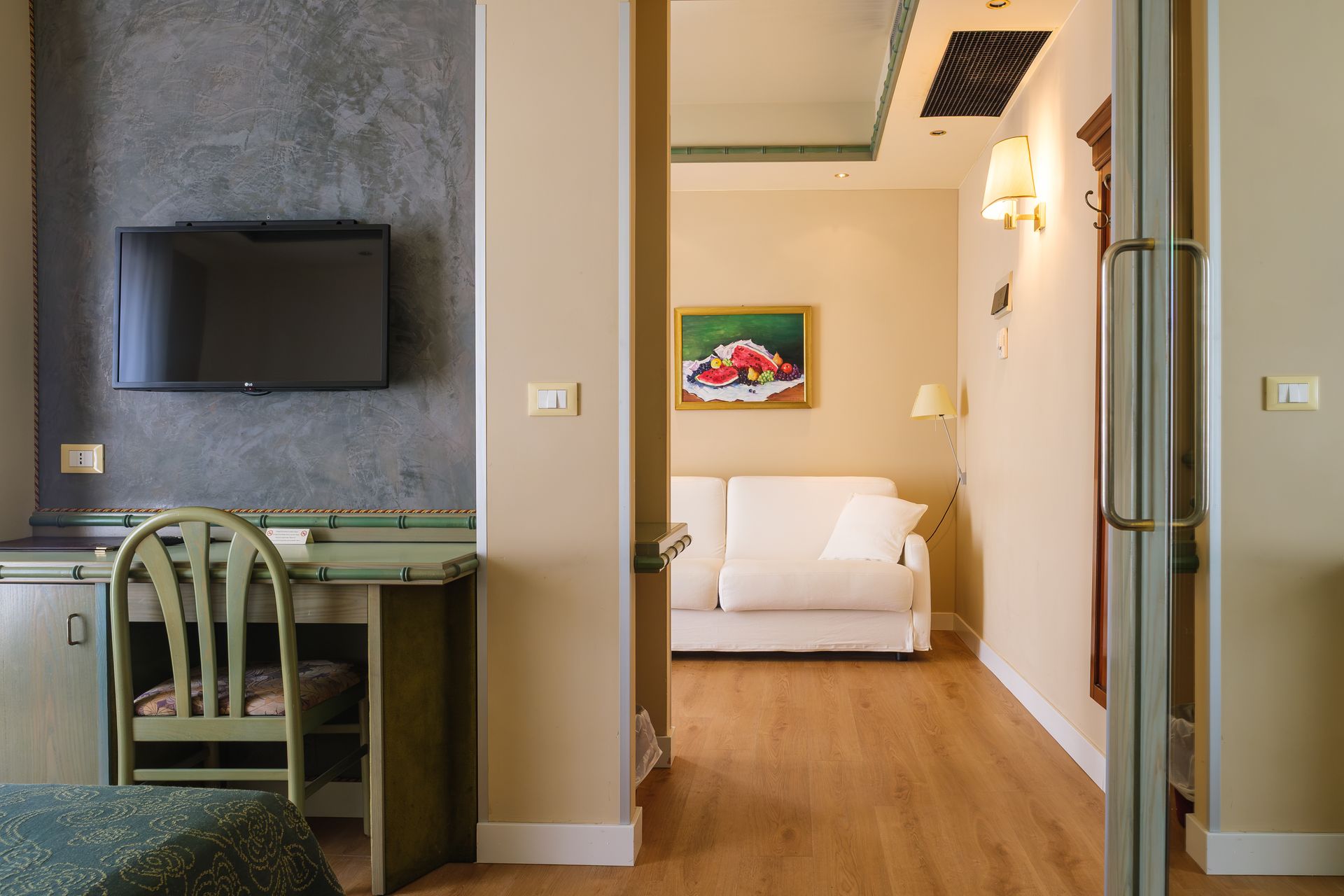 Una stanza d'albergo con un divano, una scrivania, una sedia e una televisione.