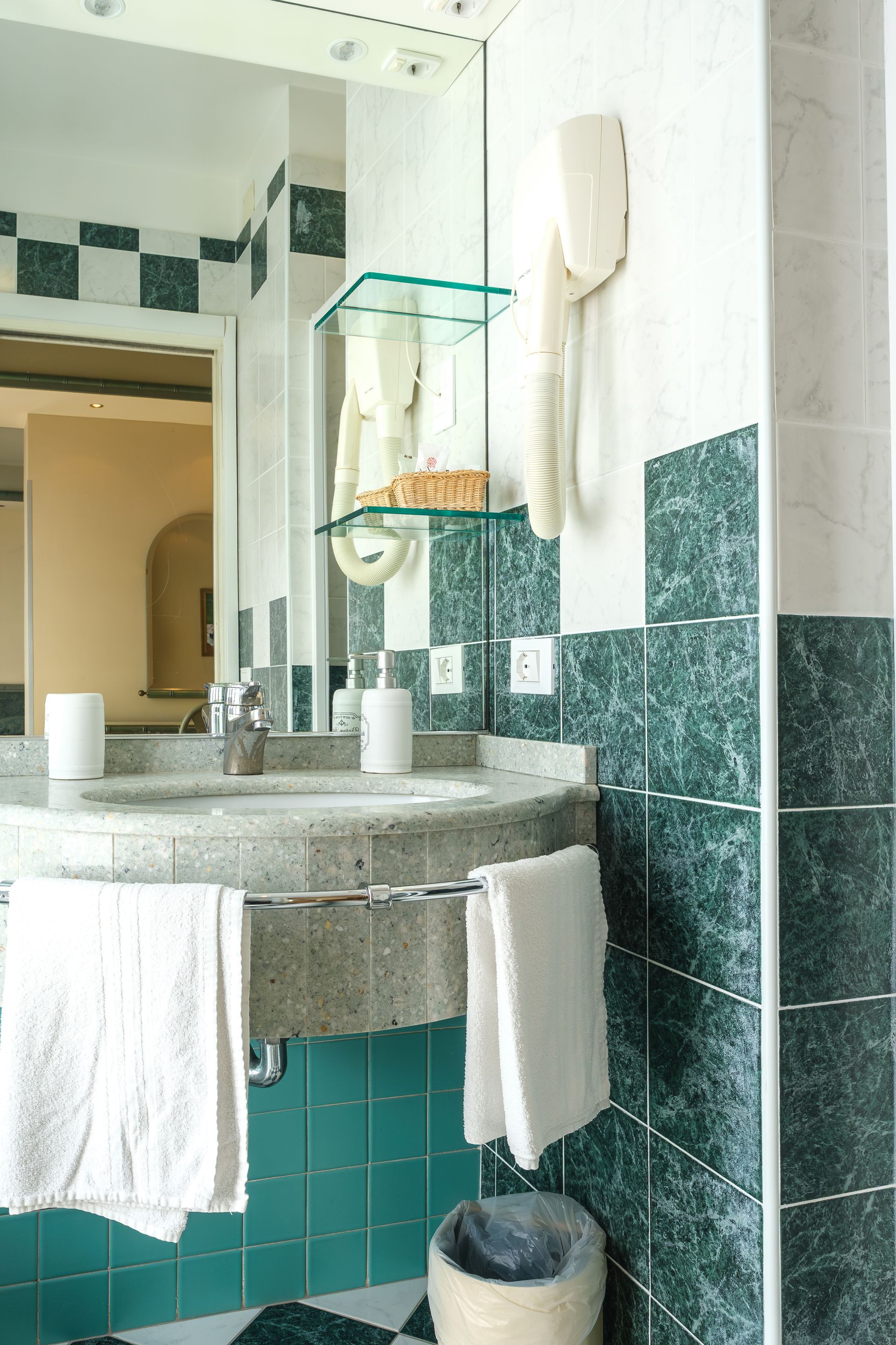 Un bagno con lavandino, specchio, asciugamani e cestino.