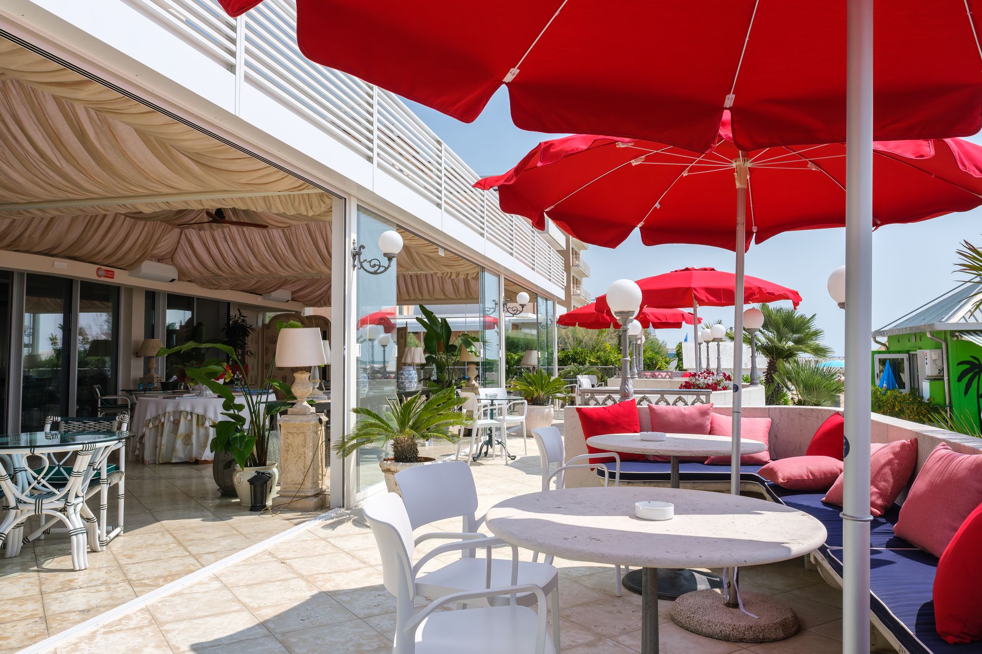 Un ristorante con ombrelloni rossi e sedie bianche.