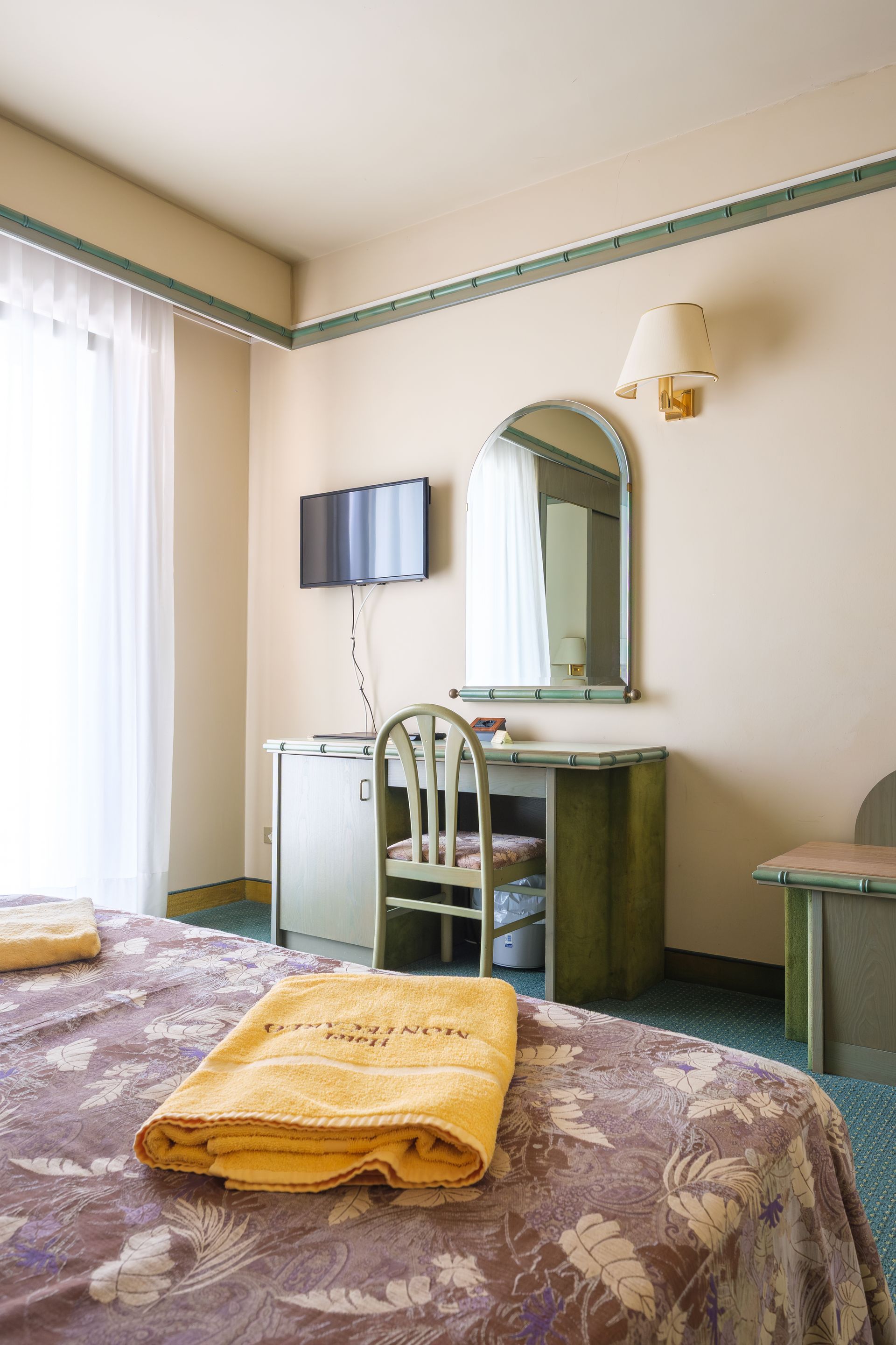 Una camera d'albergo con un letto, una scrivania, una sedia e una televisione.