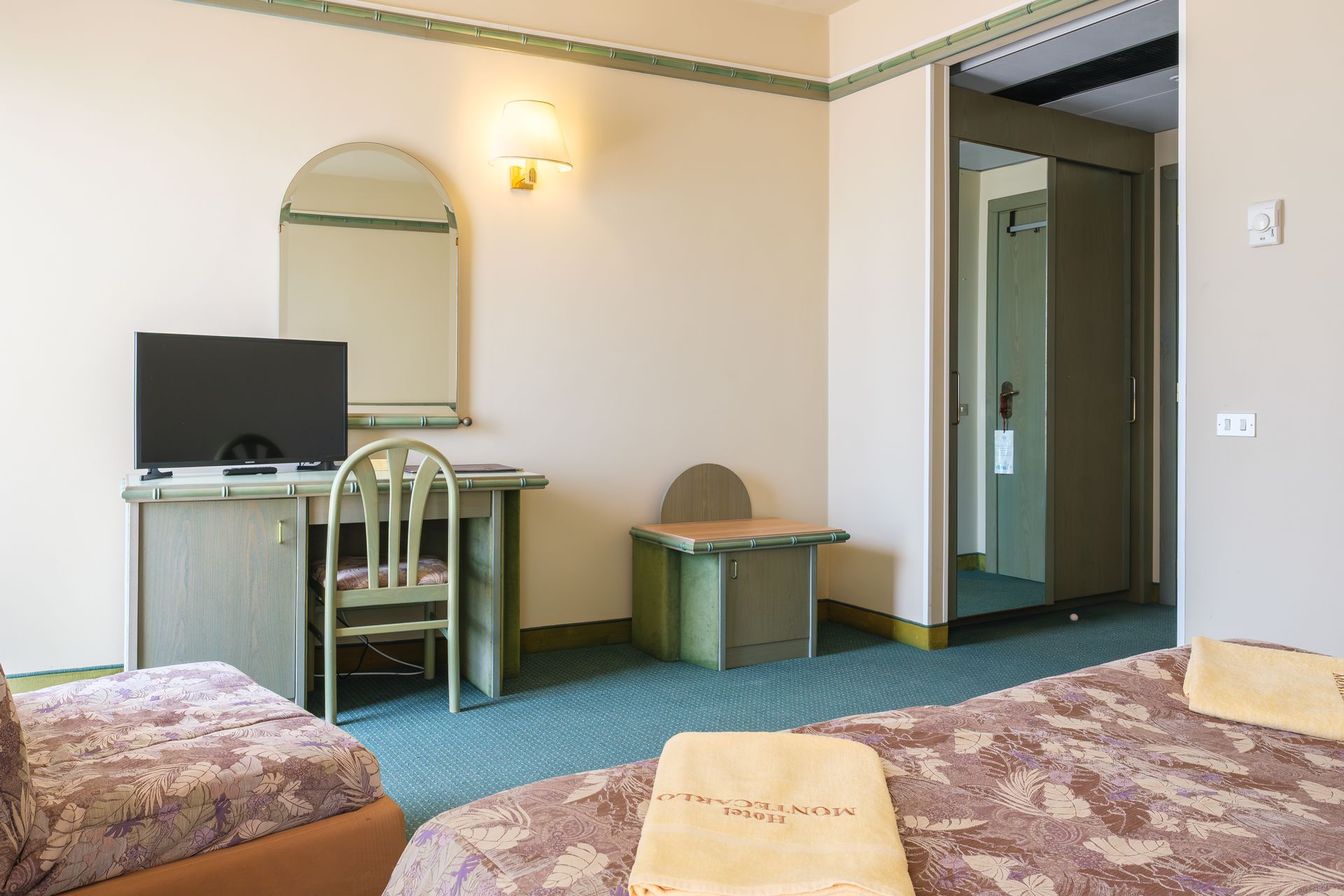 Una camera d'albergo con due letti, una scrivania, una televisione e uno specchio.