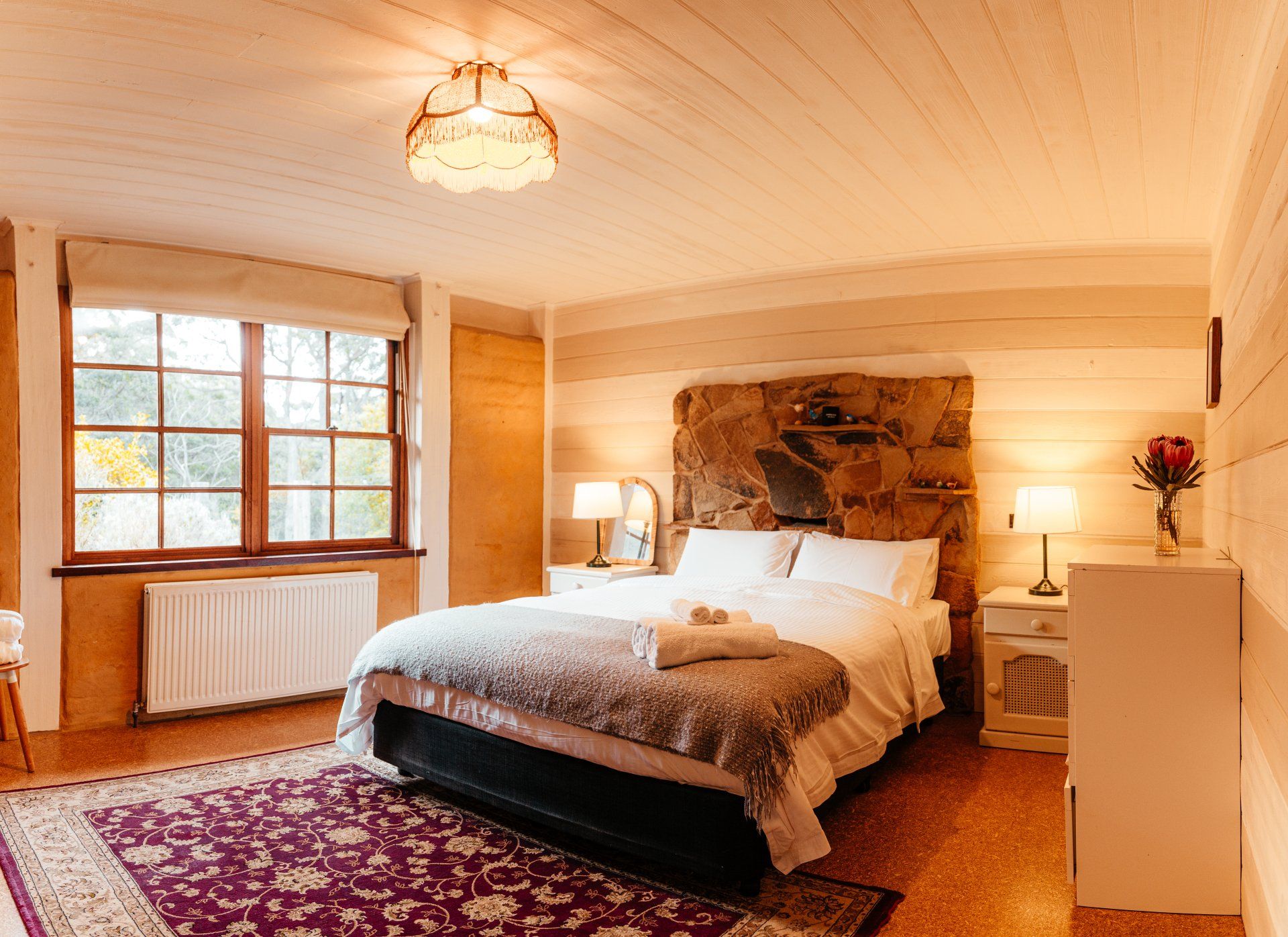 Bedroom with queen bed and garden views at The Top House, Glenaire Cottages stone wall feature 