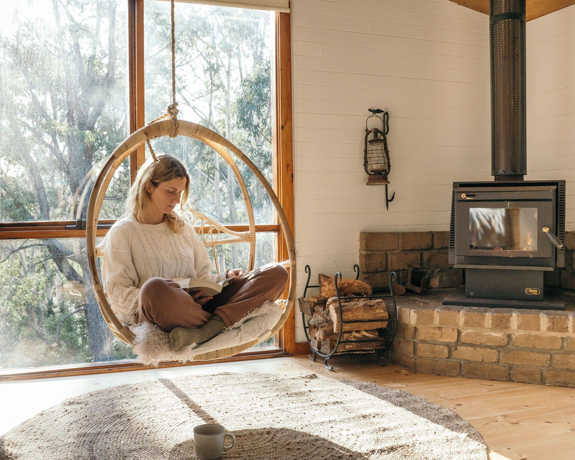 Cosy lounge with wood fire and hanging chair at Cape Cottage