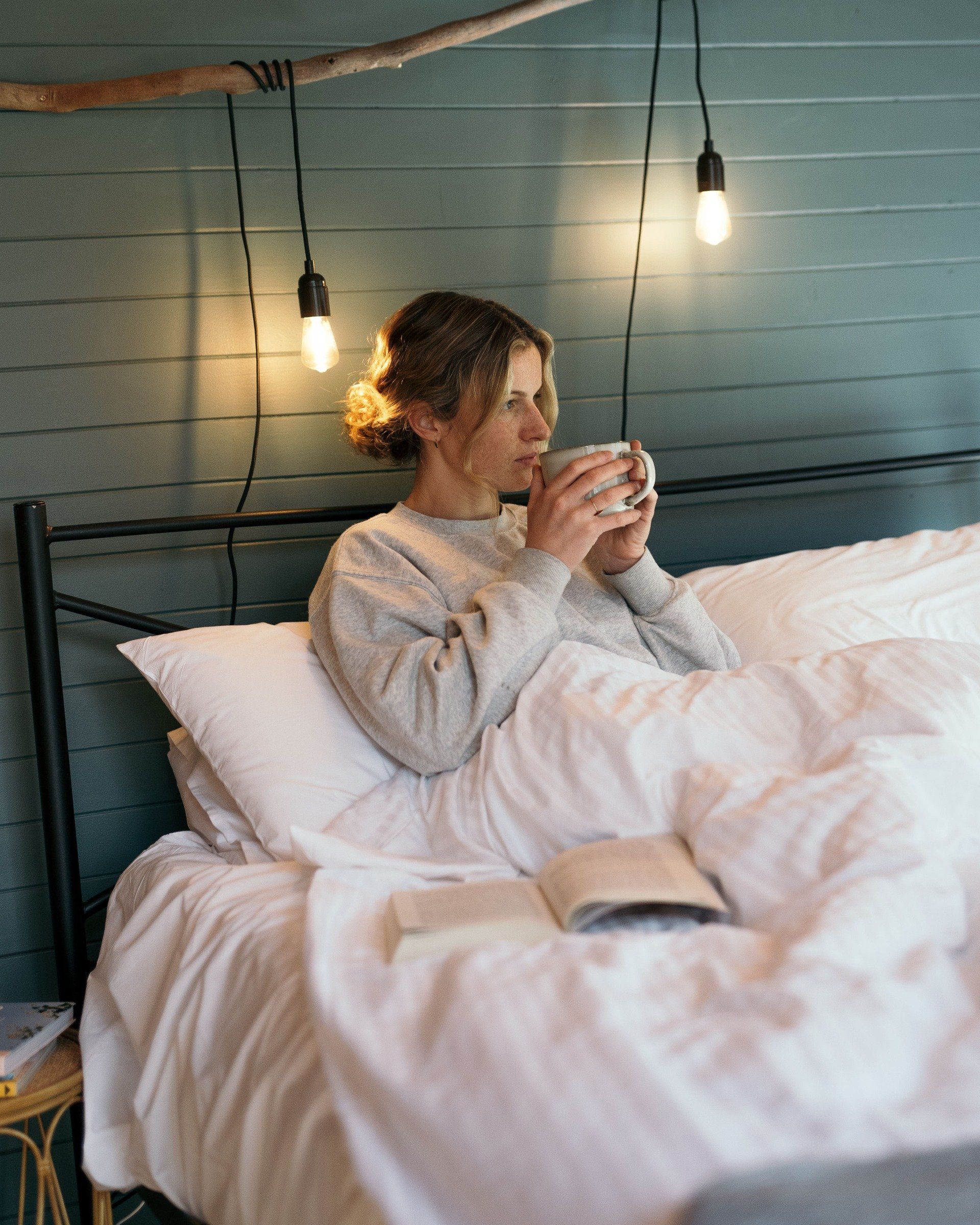 Woman relaxing in bed with a hot drink at Cape Cottage