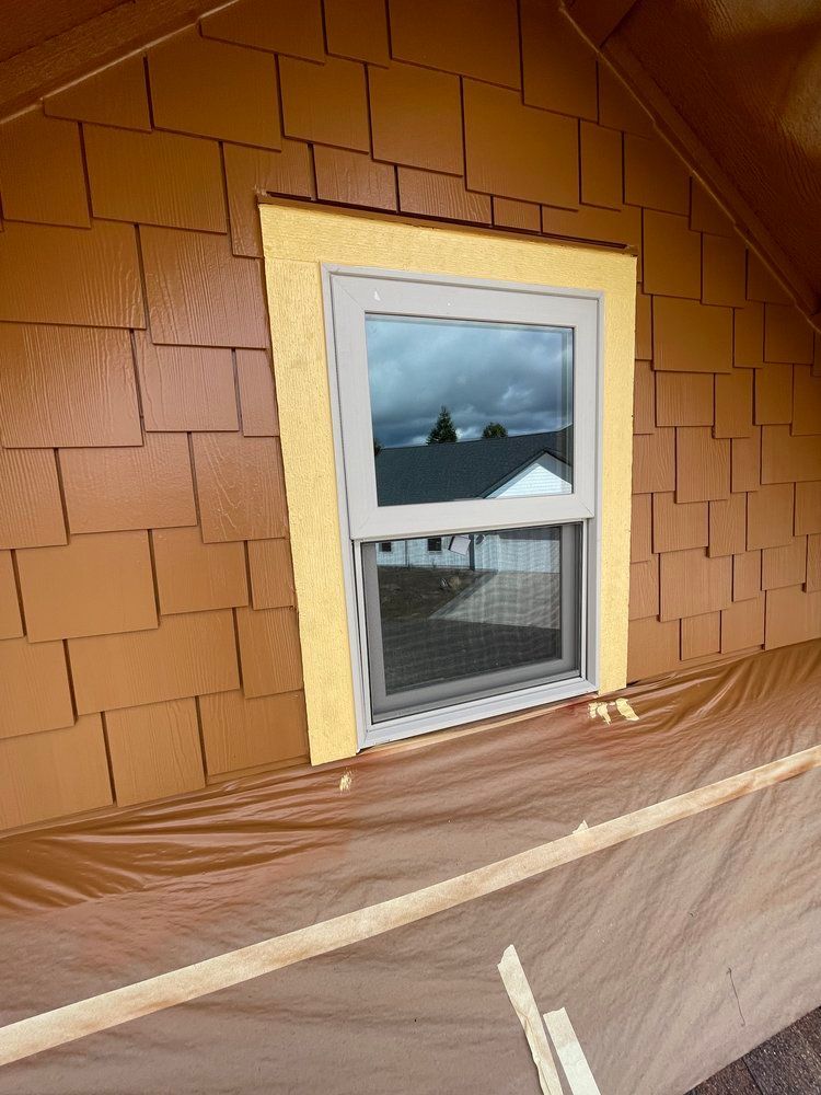 A window on the side of a house with a yellow trim.