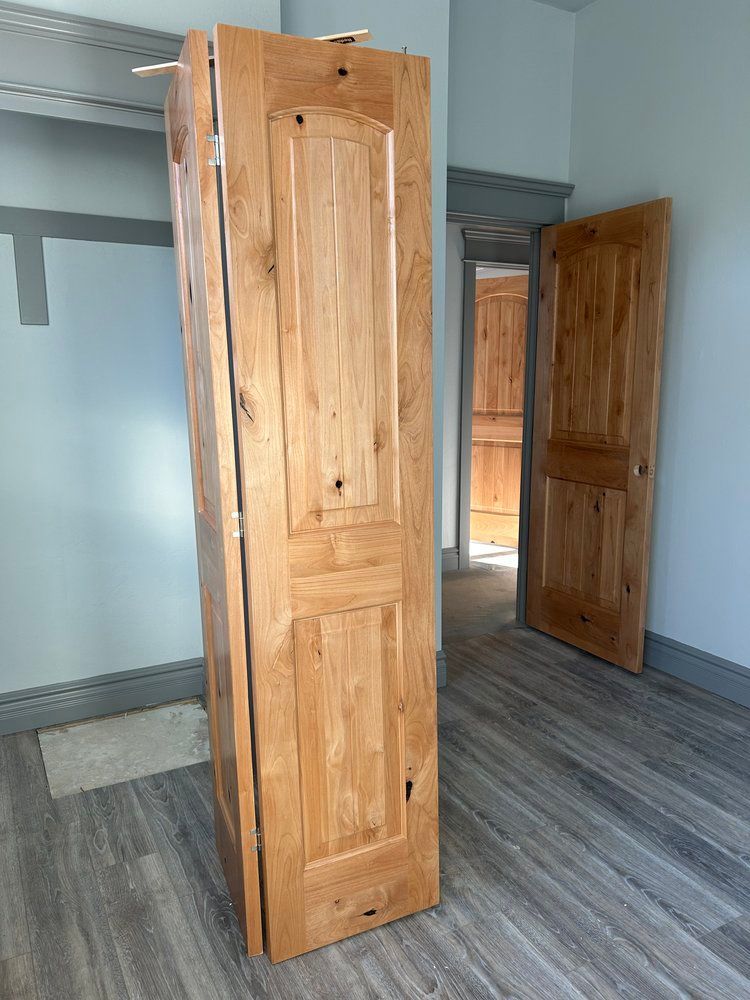 A wooden door is sitting in a room with two doors open.