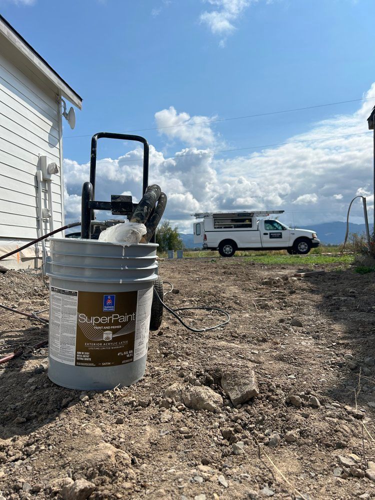 A bucket of paint is sitting on the ground in front of a house.