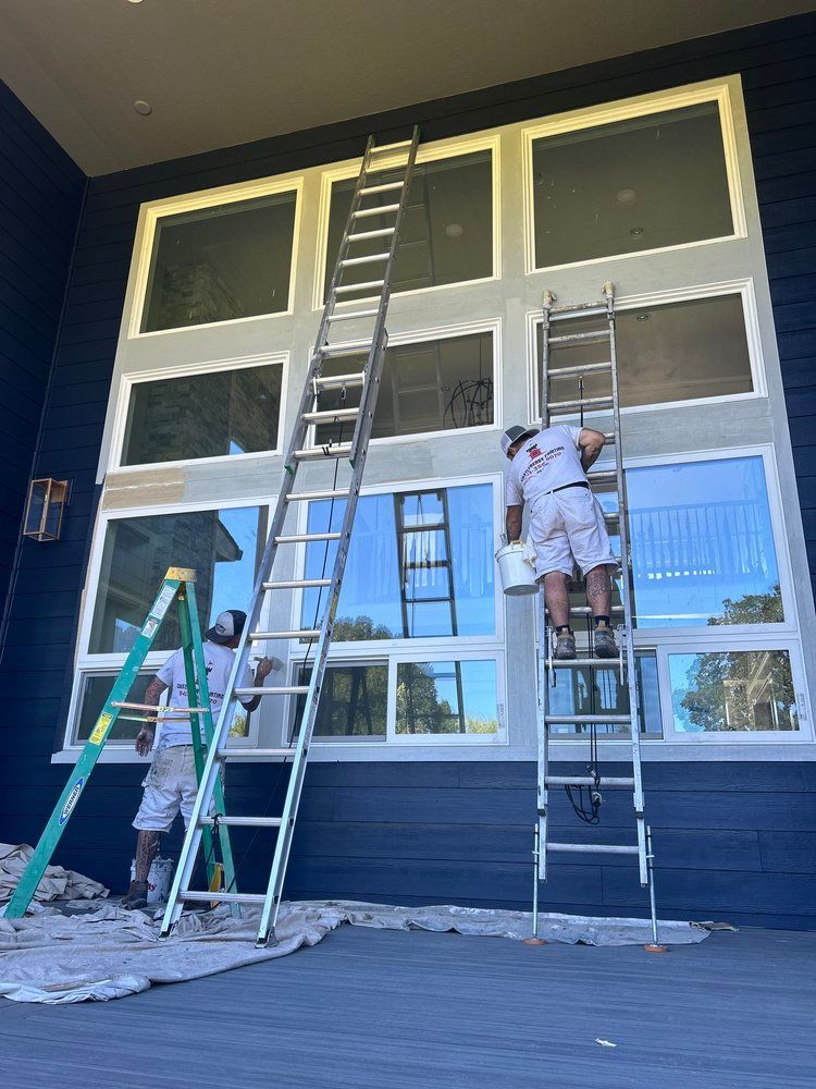 Two men are painting a large building with ladders.