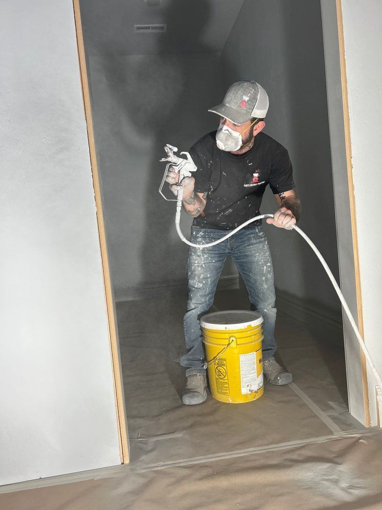 A man wearing a mask is spray painting a wall next to a yellow bucket