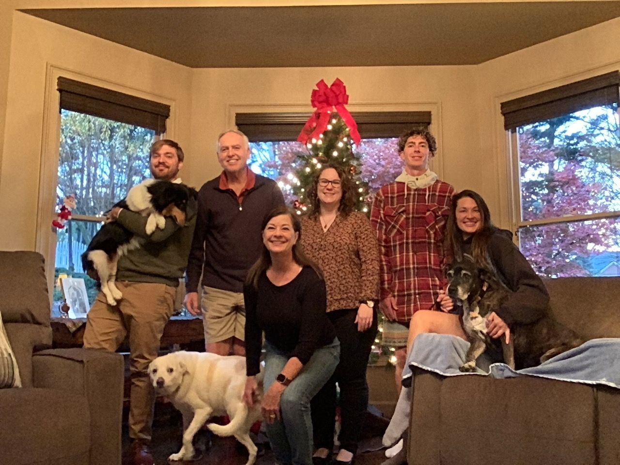 Six people and two dogs pose in a cozy living room decorated with a red bow