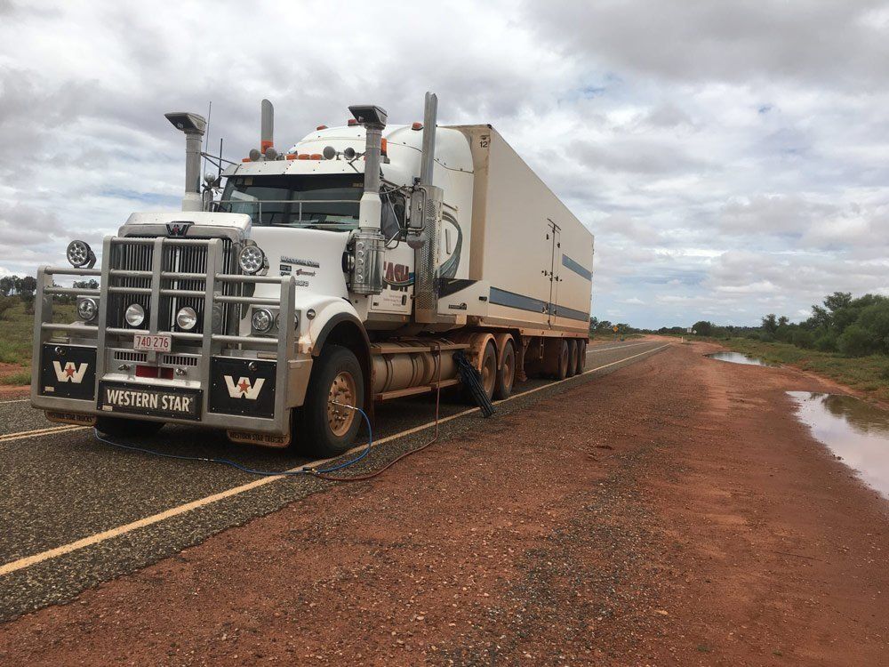 White Semi-Truck on A Red Dirt Road with Cloudy Sky — Central Australian Sidelifter Haulage in Ciccone, NT