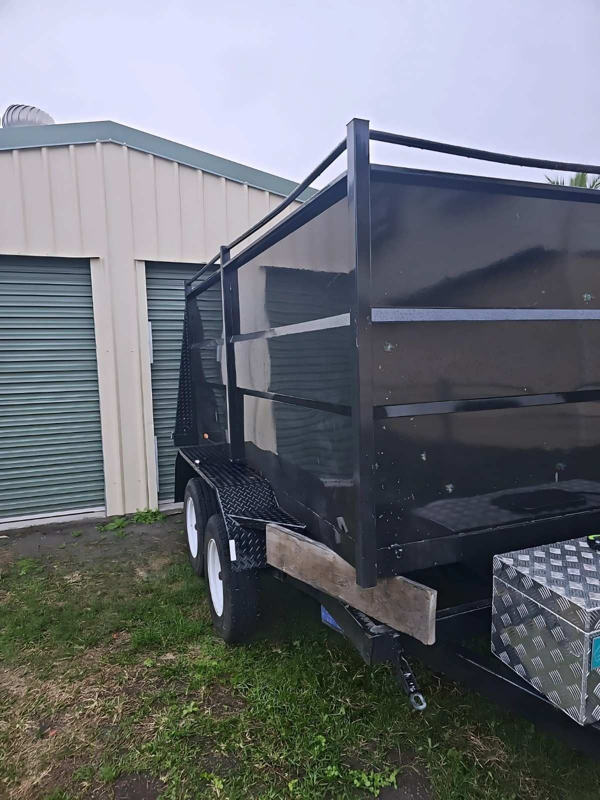 Black Utility Trailer With Cage Near Storage Units on a Green Lawn — NPX Solutions In Moranbah, QLD