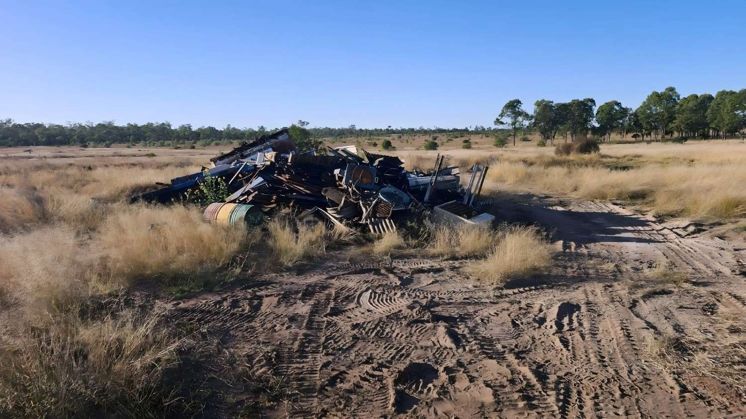 Pile of Metal Debris in a Grassy Field With Trees, Under a Clear Blue Sky — NPX Solutions In Moranbah, QLD