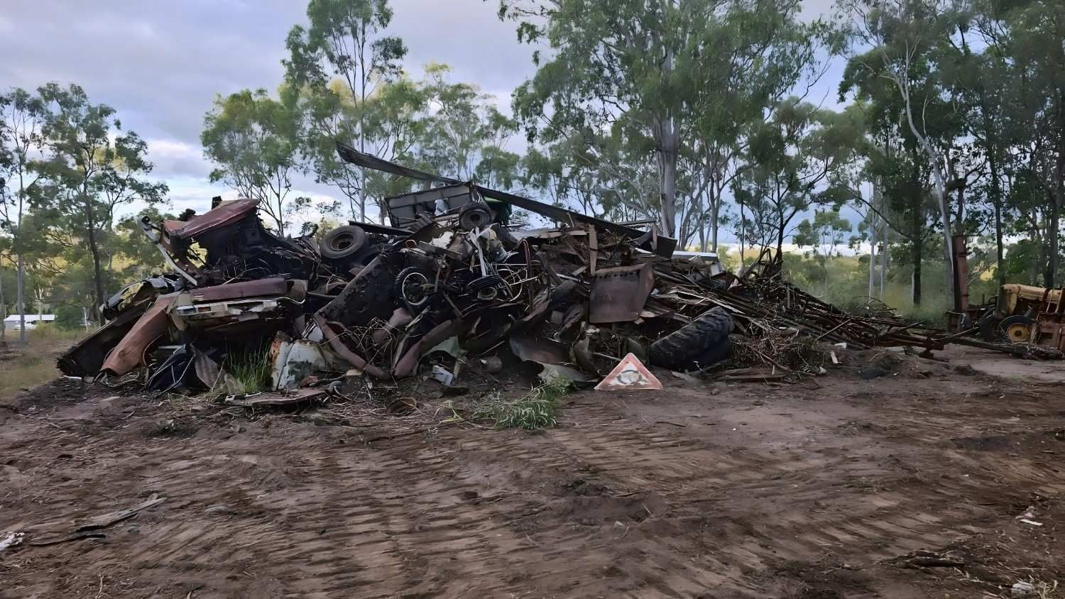 Pile of Scrap Metal in a Dirt Field, Trees in the Background, Cloudy Sky — NPX Solutions In Bundaberg, QLD