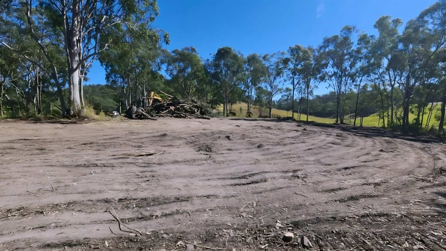 An Empty Dirt Lot Surrounded by Trees Under a Clear Blue Sky — NPX Solutions In Gympie, QLD