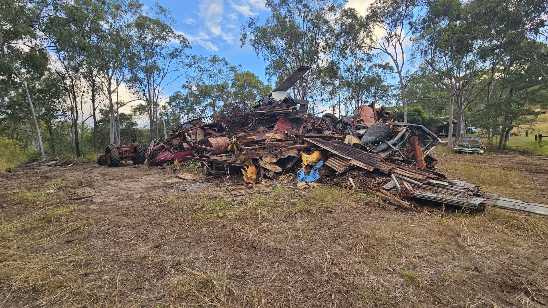 Pile of Burned Debris in a Grassy Field, Surrounded by Trees Under a Cloudy Sky — NPX Solutions In Gympie, QLD