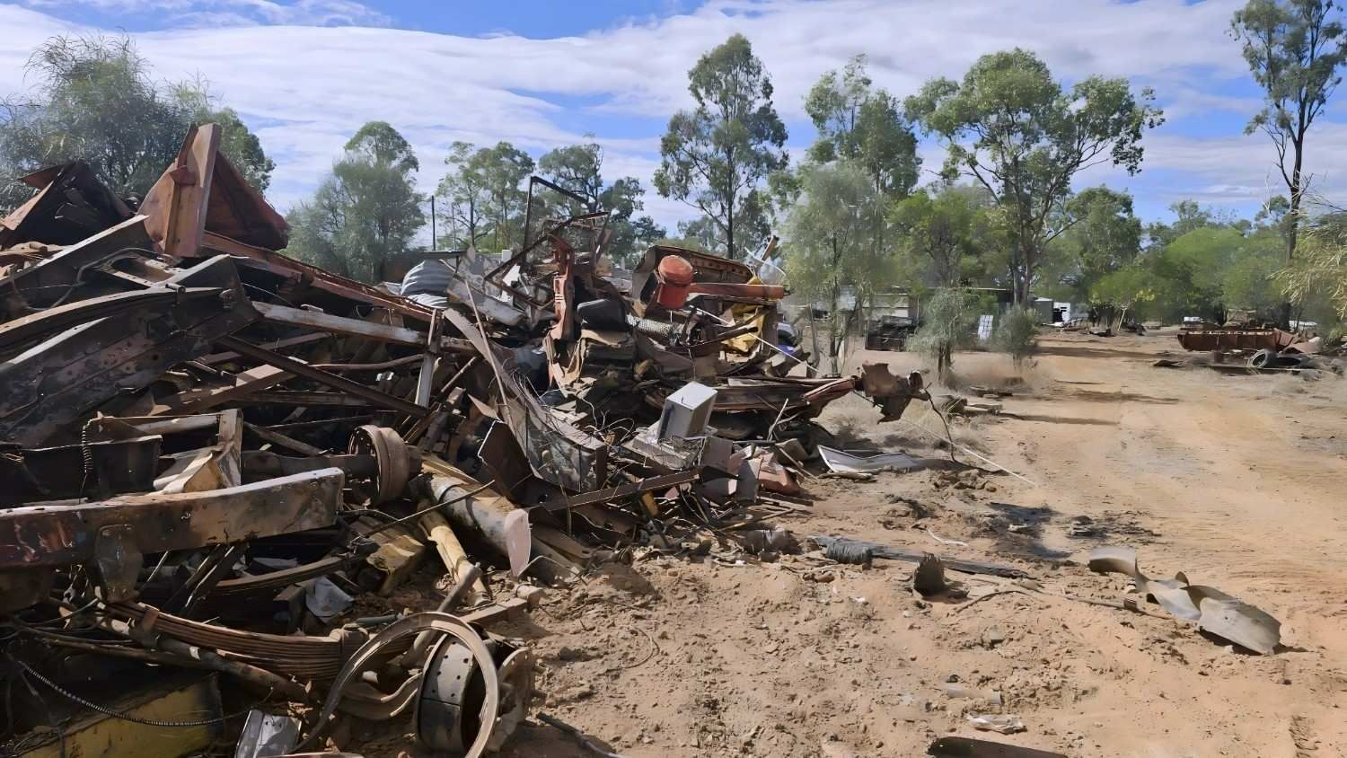 Pile of Scrap Metal and Debris Beside a Dirt Road, Trees in Background Under Blue Sky — NPX Solutions In Gympie, QLD