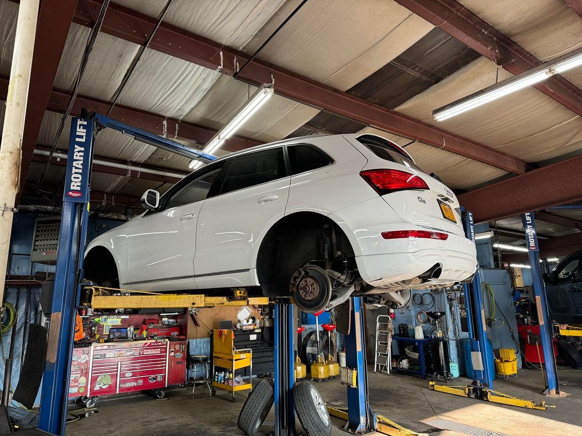 White SUV on a lift in a garage, wheels removed. Tools and equipment visible.