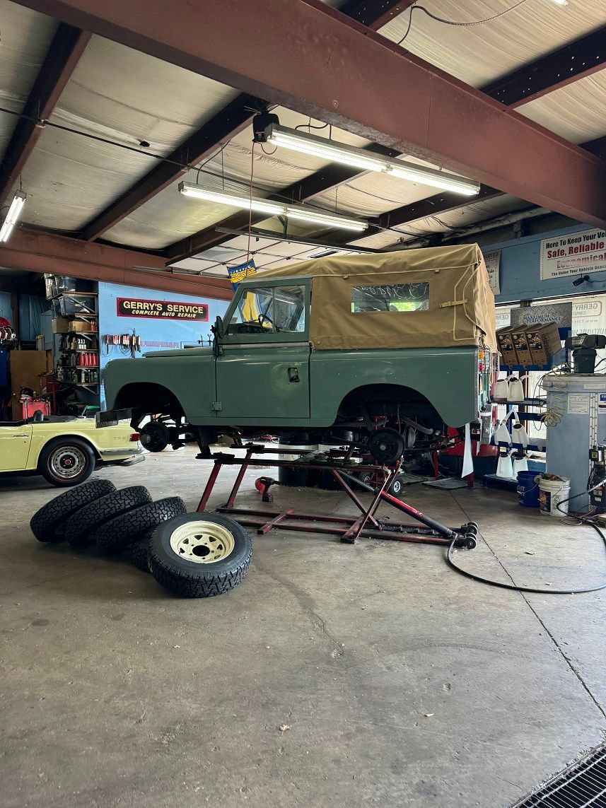 Green Land Rover on a lift in a garage, tires on the ground.