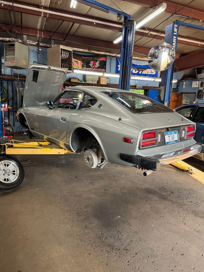 Silver Datsun 280Z on a lift in a garage, hood open. Rear wheel removed, awaiting repair.