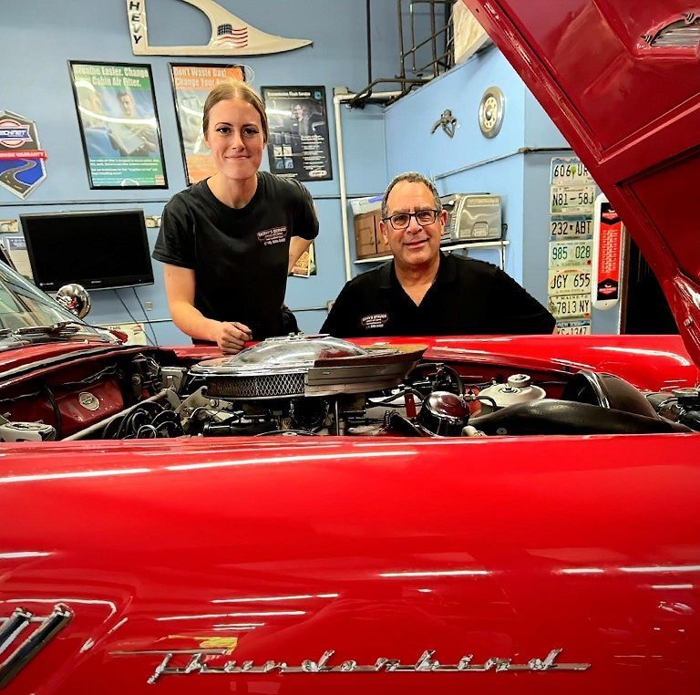Woman and man standing by a red Thunderbird with its hood open in a garage.