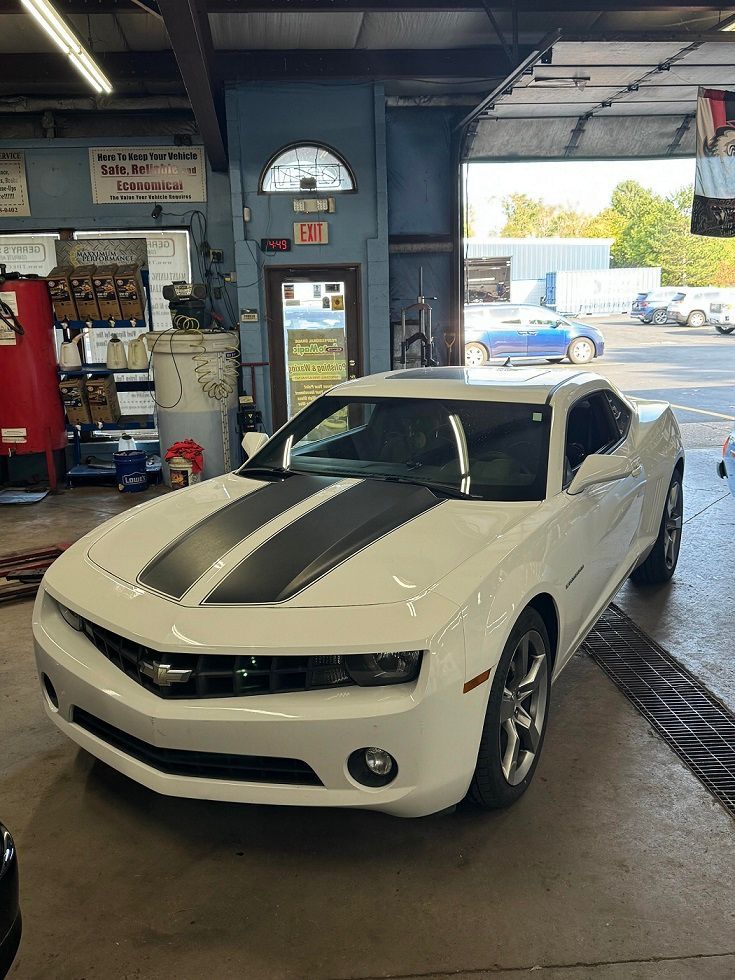 White Chevy Camaro with black stripes in an auto shop.